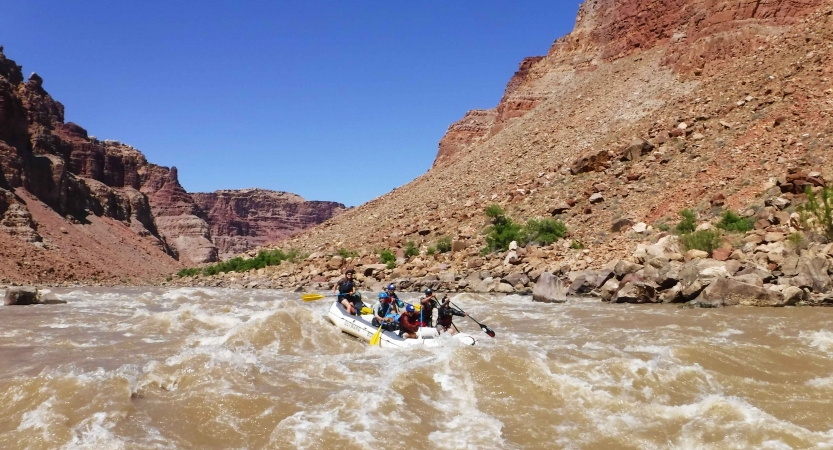 A raft is navigated through whitewater, framed by tall canyon walls.